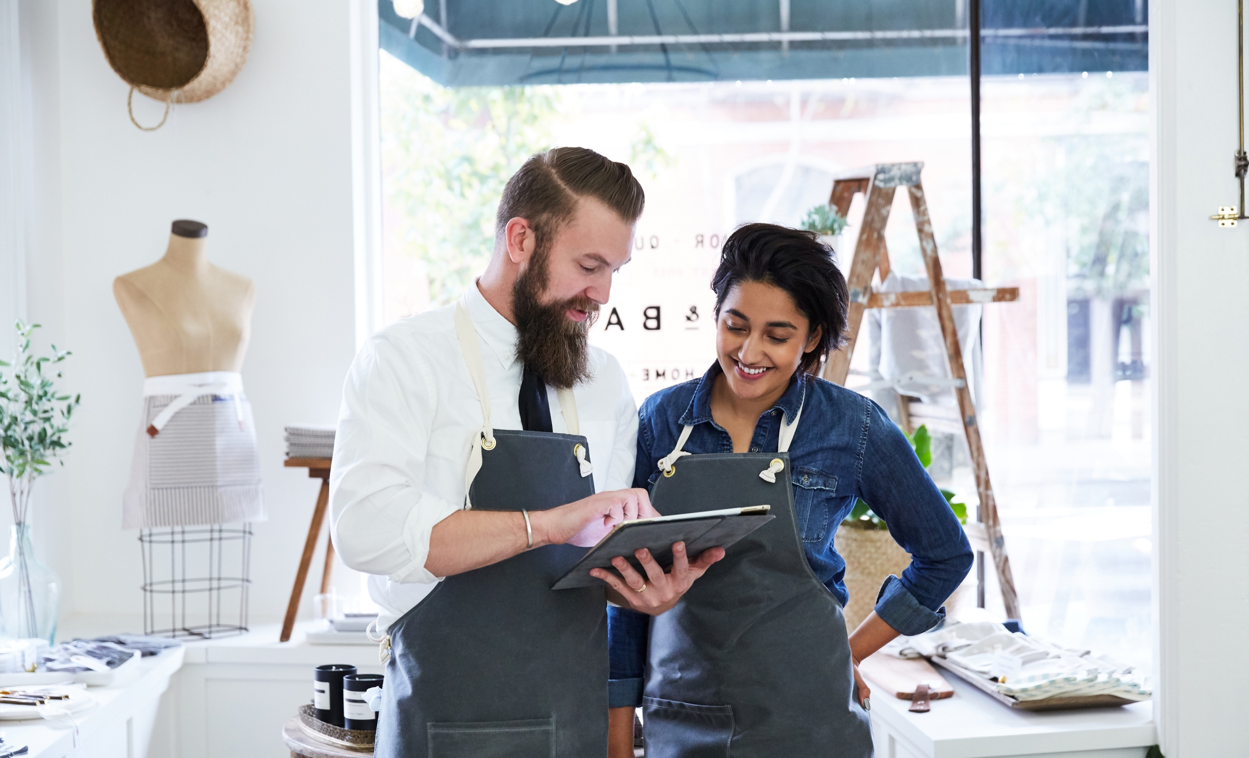 Two business owners standing in their store. One of them is holding an iPad and showing it to the other.