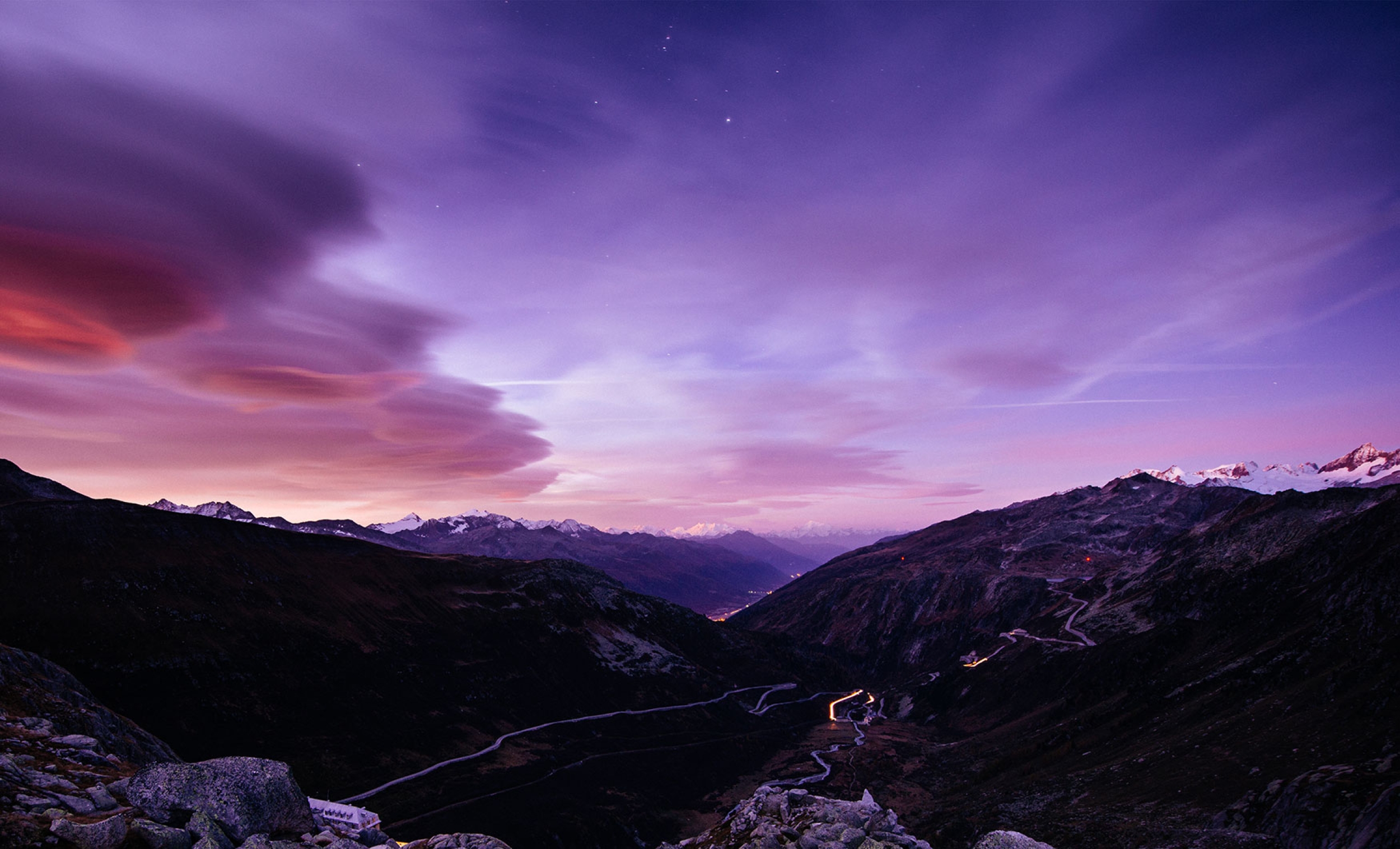 Beautiful landscape of mountains and purple and pink skies – small roads lay in the distance ahead.