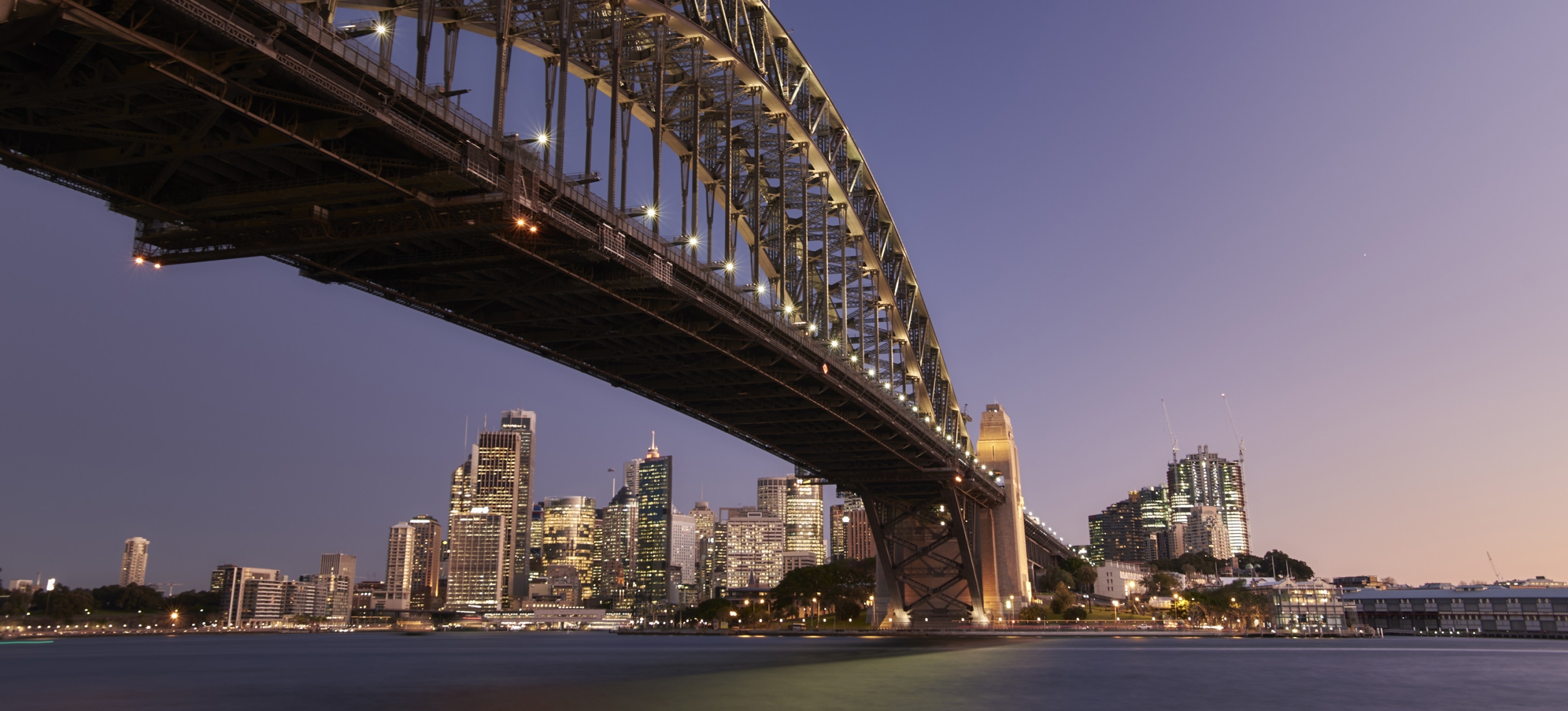A panoramic cityscape with a purple sky and the Sydney Harbour Bridge in front.