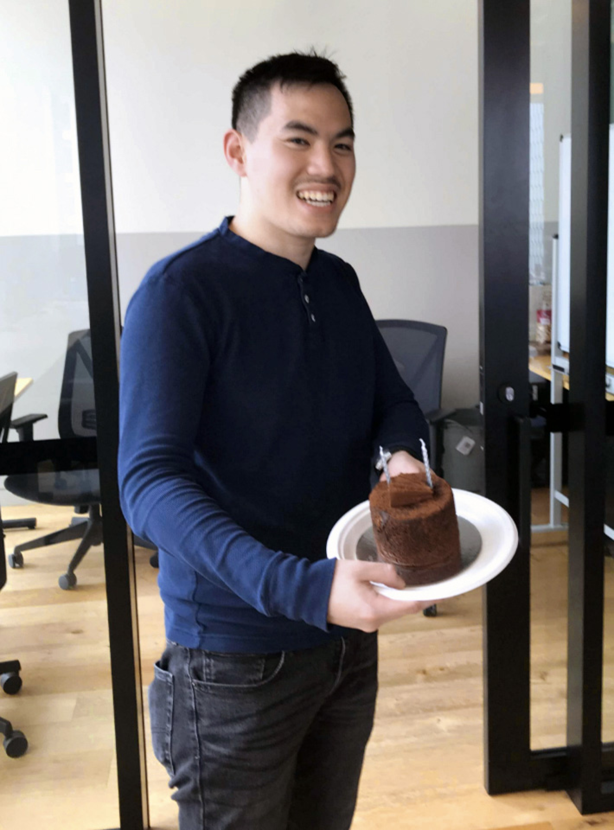 Snapshot of an mx51 employee who is posing holding a cake with birthday candles in his hands and smiling.