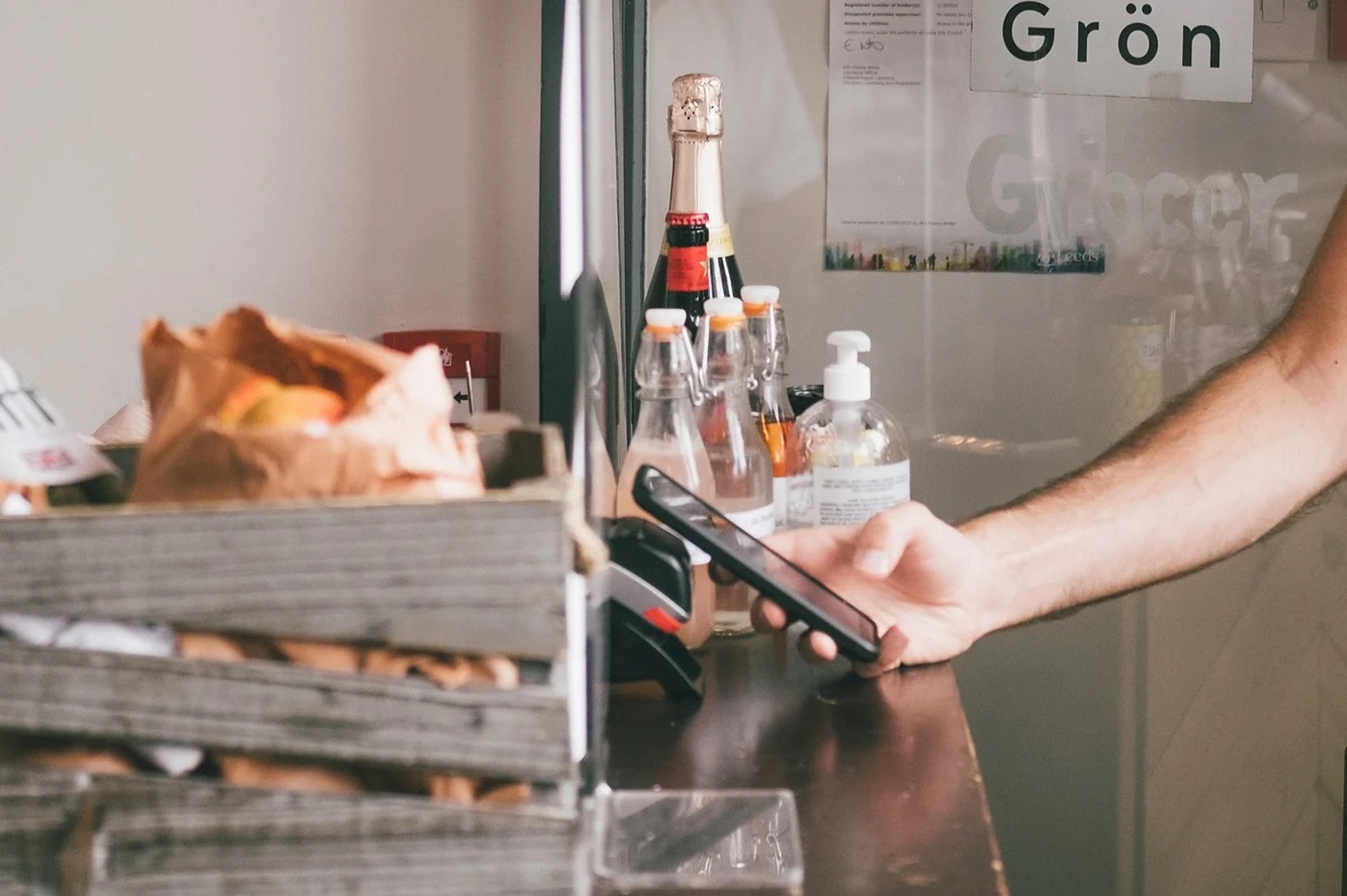 Hand holding a phone in front of a payments device in a shop to make a payment.