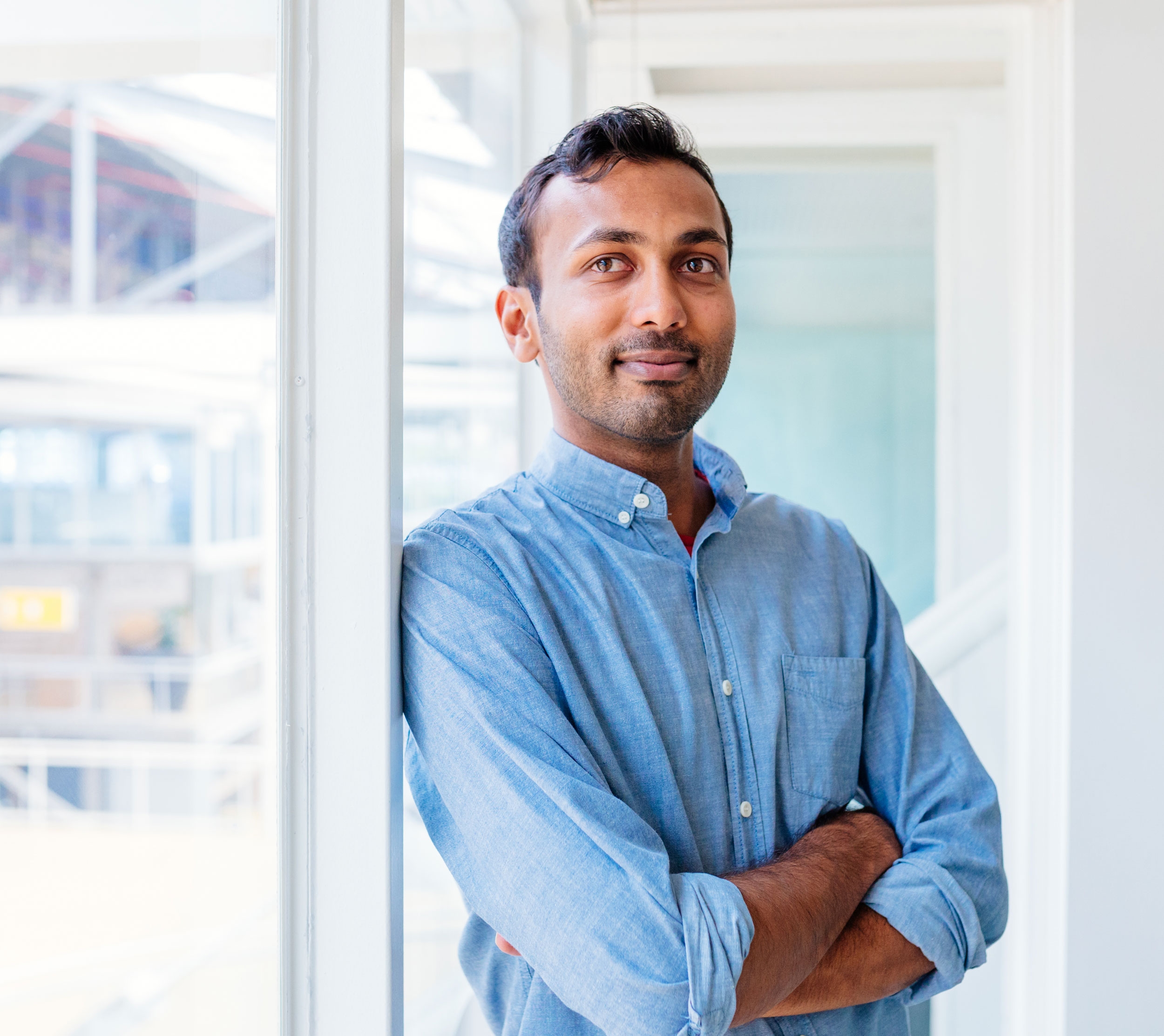 Young business man posing next to a window in an office environment.