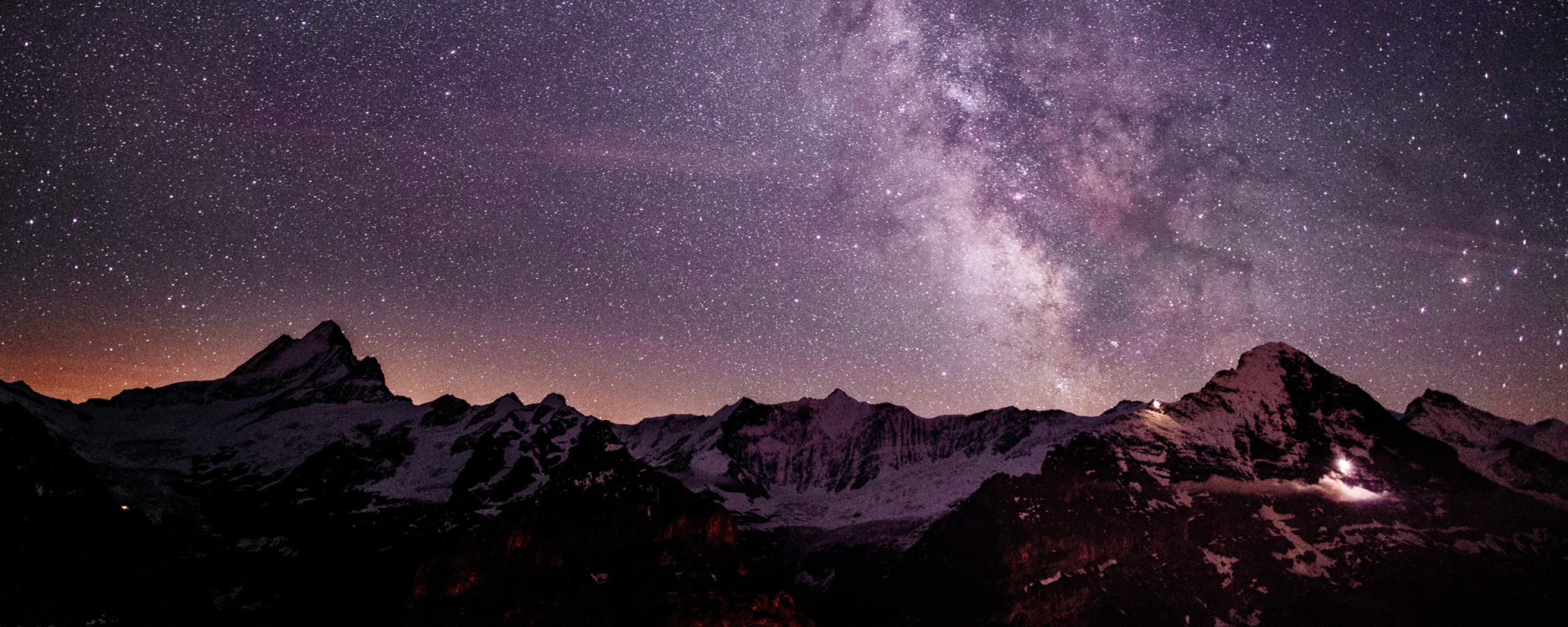 Beautiful landscape of mountains and purple and pink night skies with bright visible stars above.