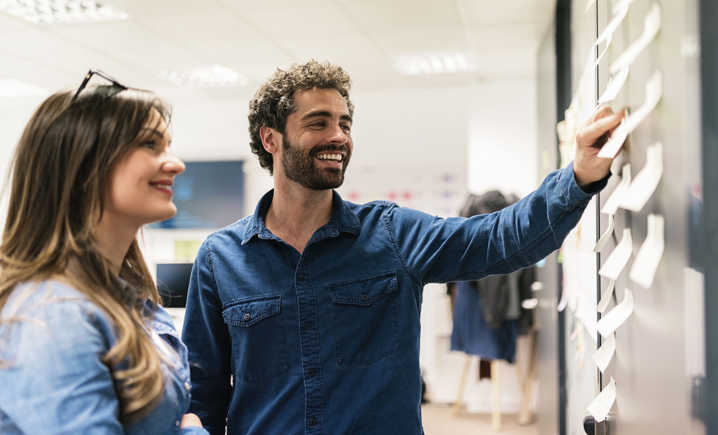 Two colleagues are smiling and looking at a blackboard with notes on them.