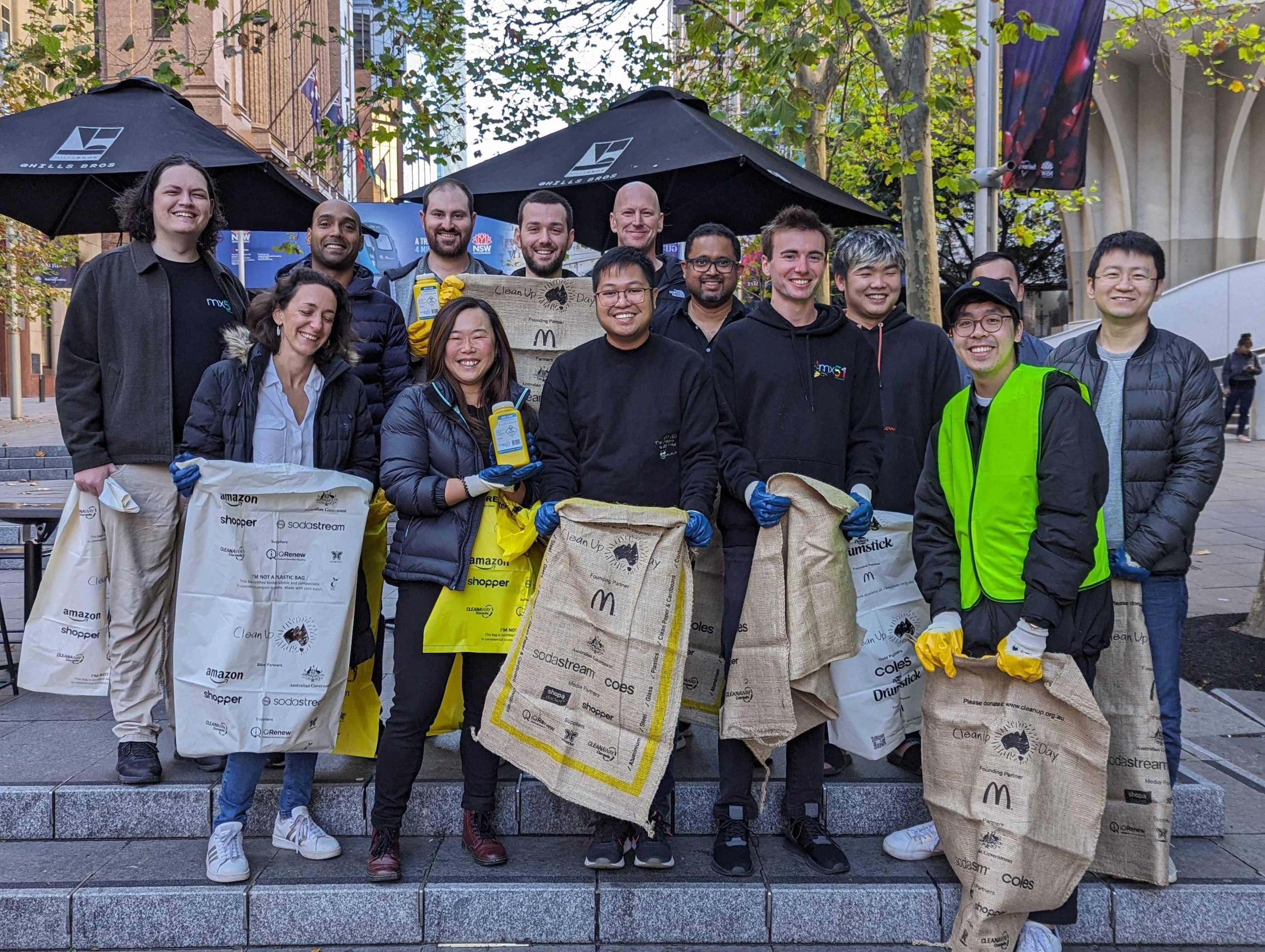 A group of 14 mx51 team members are smiling and standing with trash that they have collected whilst volunteering for Clean Up Australia.