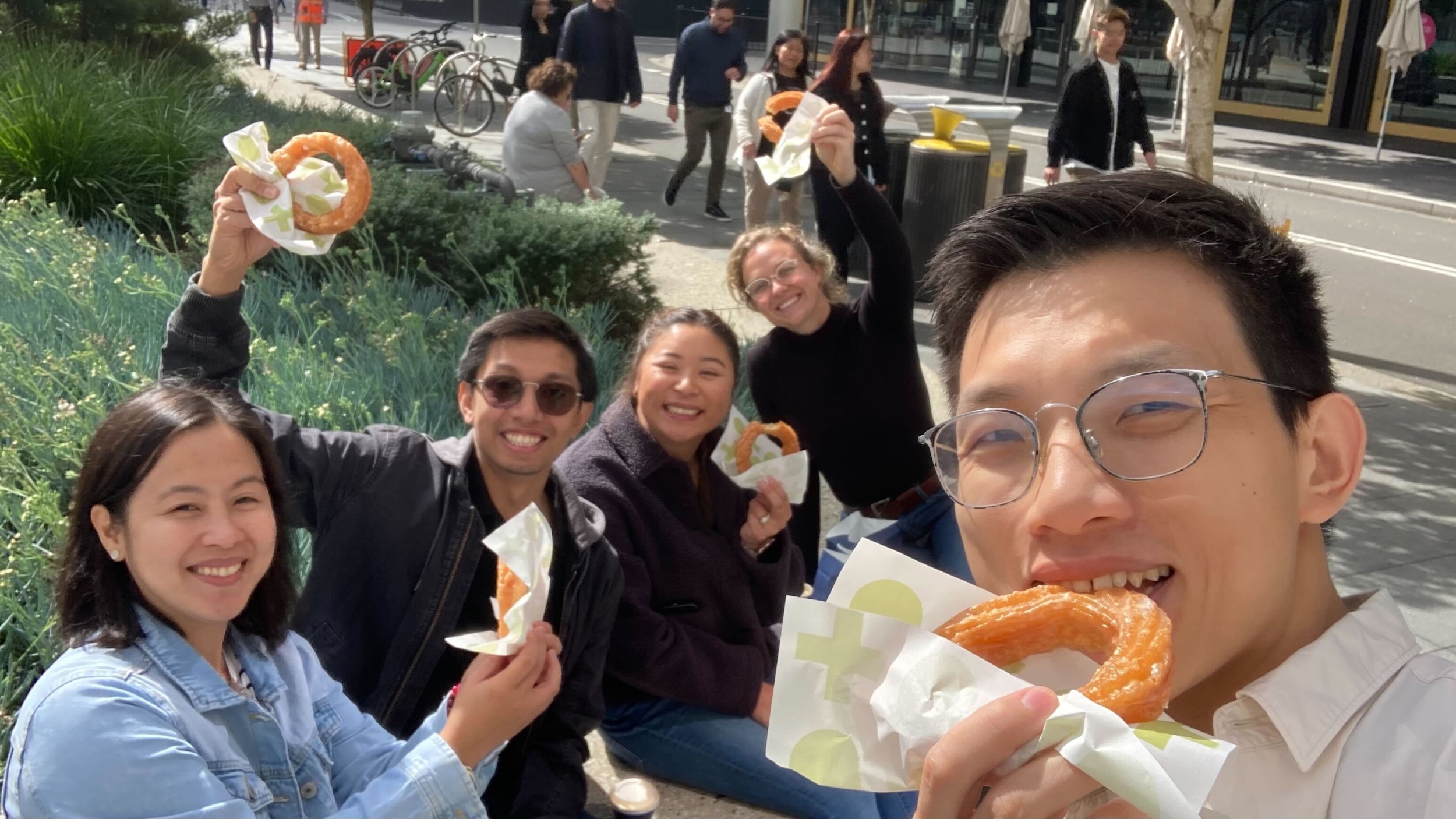 A selfie taken of a group of mx51 employees smiling and holding large cinnamon donuts.