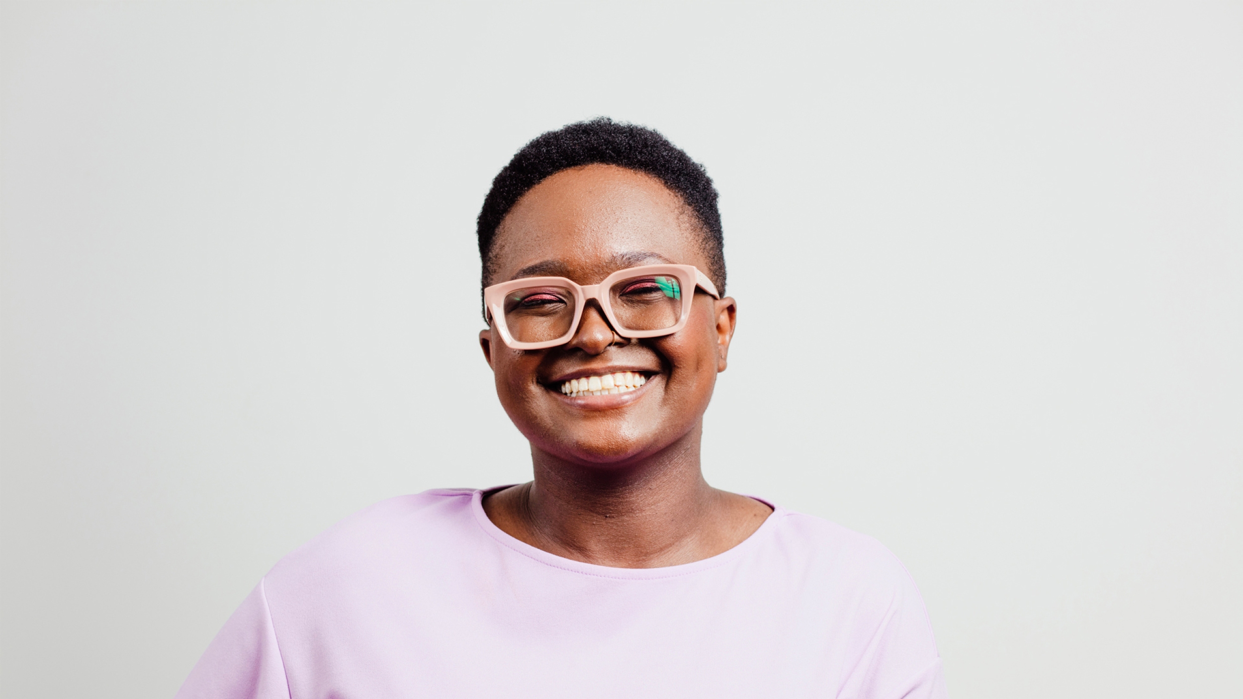 Energetic young black woman with short hair wearing a pink top and pink glasses and smiling at the camera.