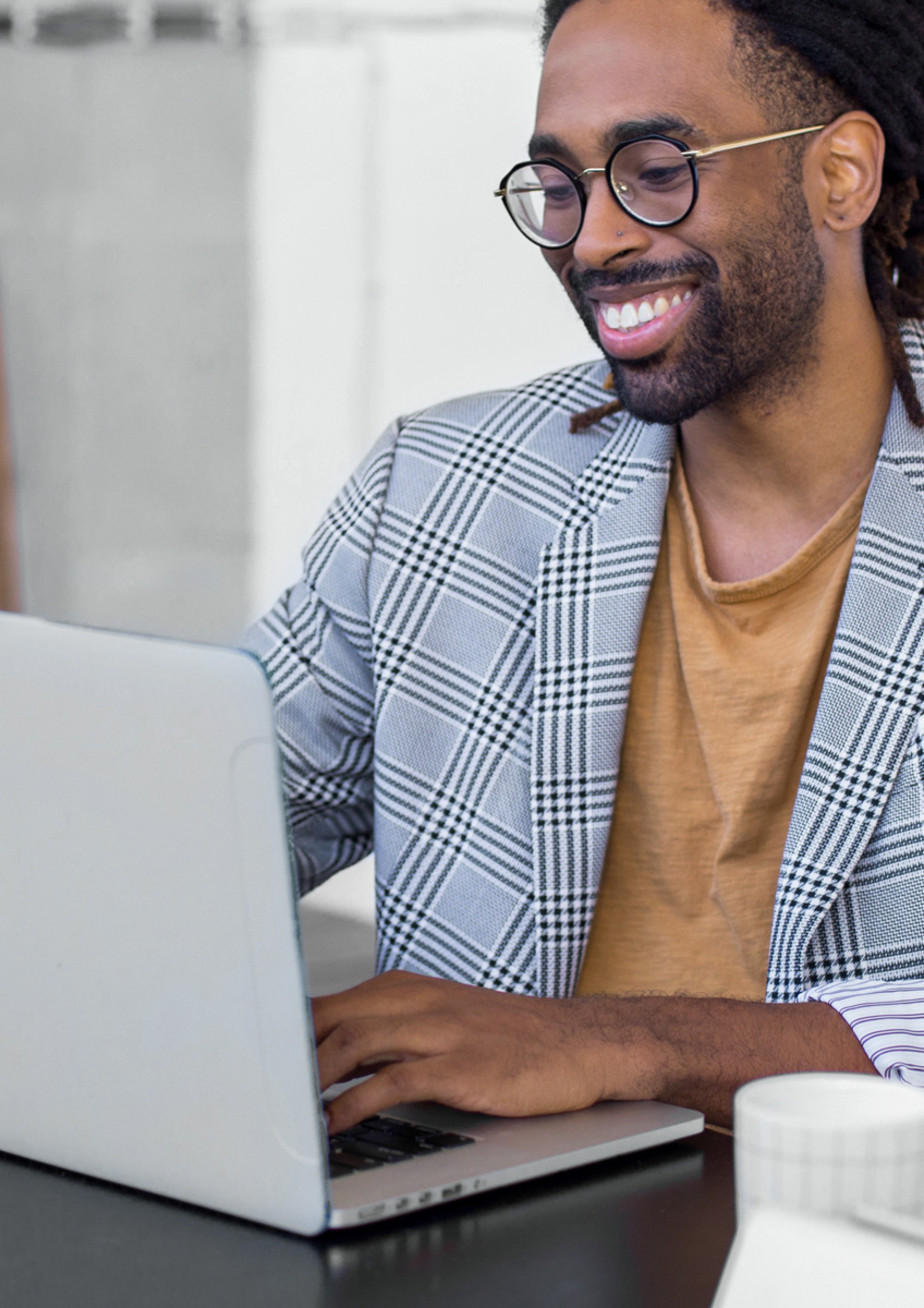 Photo of a smiling young black man wearing glasses and a blazer, looking at his laptop.